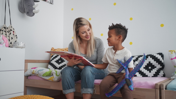 A mid adult mother reading book to her little multiracial son at home, hugging and kissing him.