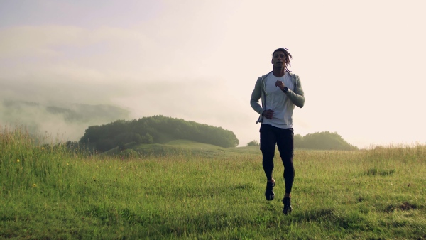 Front view of young mixed race man doing exercise on meadow outdoors in nature.