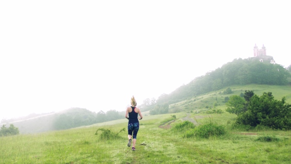 A rear view of young woman running on meadow outdoors in foggy nature.