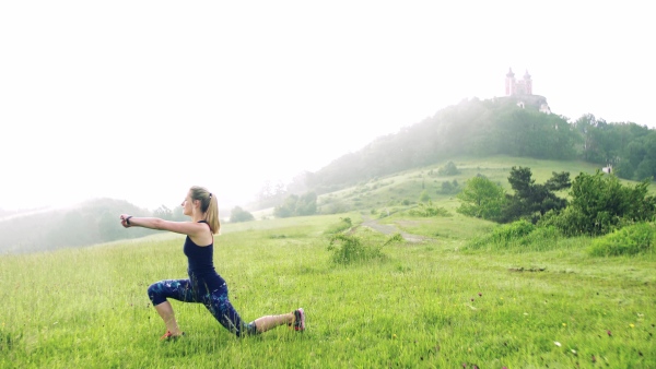 Side view of young woman doing exercise on meadow outdoors in nature early in the morning.