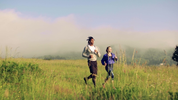 Young couple running on meadow outdoors in nature, early in foggy morning.