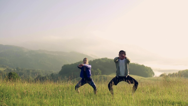 Front view of young couple doing exercise on meadow outdoors in nature early in the morning.