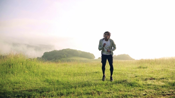 Front view of young mixed race man doing exercise on meadow outdoors in nature. Slow motion.