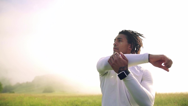 A young mixed race man doing exercise on meadow outdoors in nature, stretching. Slow motion.