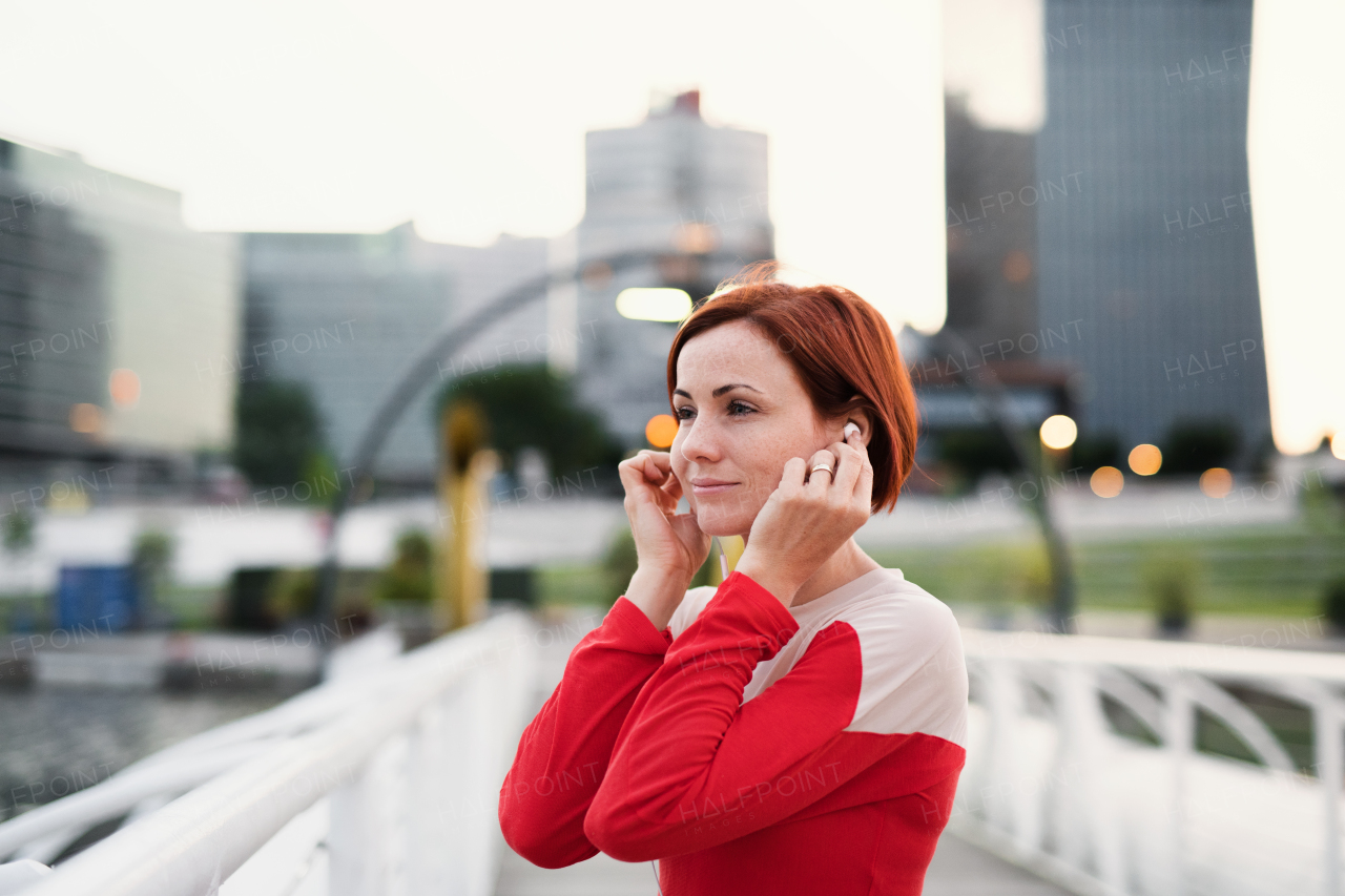 A young woman runner with earphones in city, resting on the bridge.