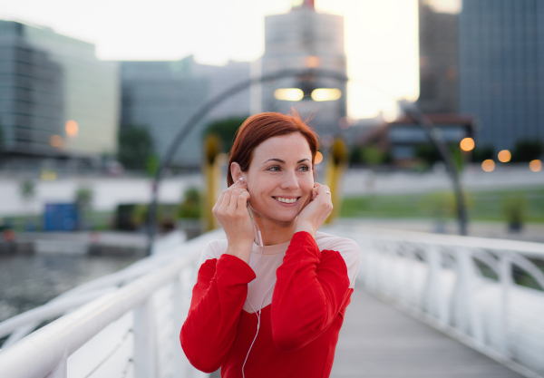 Front view of young woman runner with earphones in city, resting on the bridge.