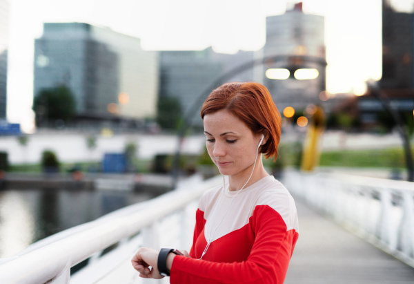 A young woman with smartwatch on bridge outdoors in city, resting after exercise.