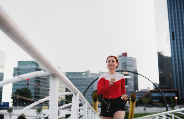 Front view of young woman runner with earphones jogging outdoors in city.