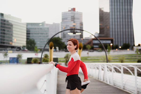 A young woman doing exercise on bridge outdoors in city, stretching.