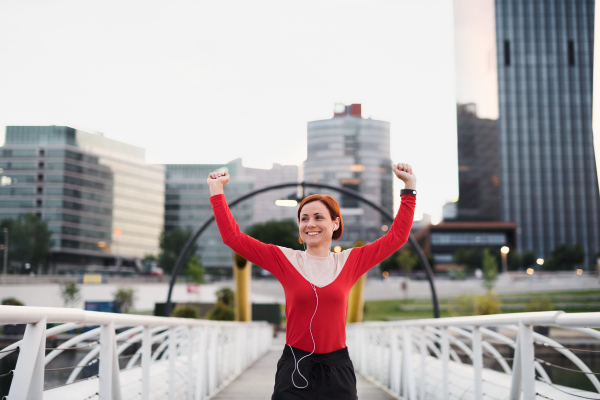 Front view of young woman runner with earphones in city, resting on the bridge.