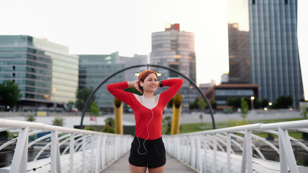 Front view of young woman runner with earphones in city, resting on the bridge.