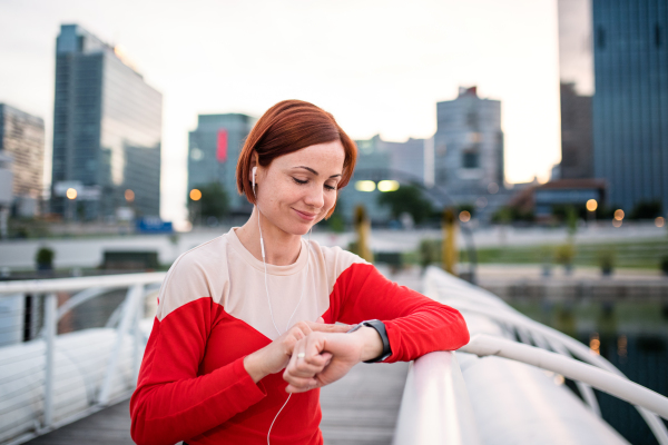 Young woman runner with earphones in city, using smartwatch when resting.