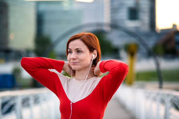 Front view of young woman runner with earphones in city, resting on the bridge.