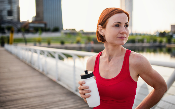 Young woman runner with water bottle in city, resting on the bridge. Copy space.