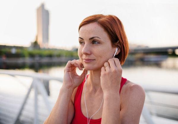 Front view of young woman runner with earphones in city, resting on the bridge.