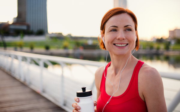 Young woman runner with water bottle in city, resting on the bridge. Copy space.