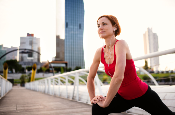 Young woman runner with earphones in city, stretching on the bridge. Copy space.