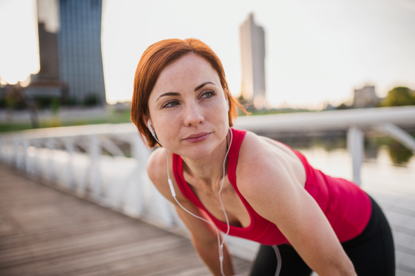 Young woman runner with earphones in city, resting on the bridge. Copy space.