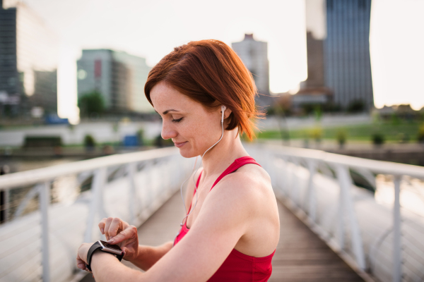 A young woman with smartwatch on bridge outdoors in city, resting after exercise.