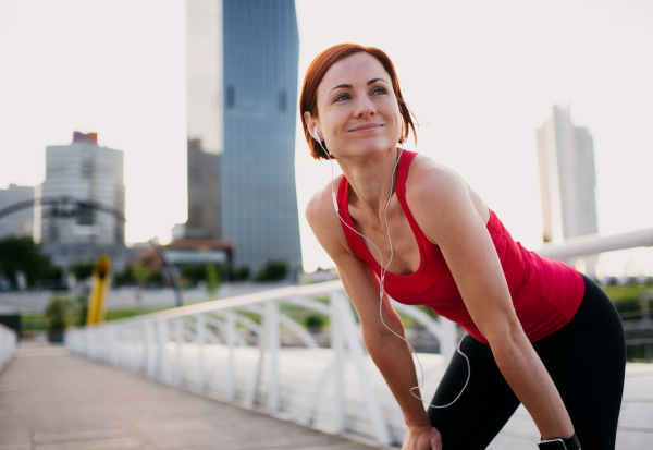 Young woman runner with earphones in city, resting on the bridge. Copy space.