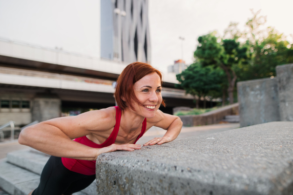 Young woman doing exercise outdoors in city, push-ups.