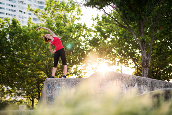 A young woman doing exercise outdoors in city, stretching.