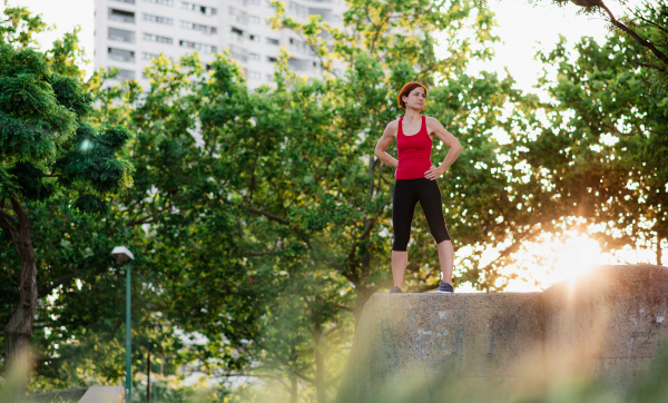 A young woman standing outdoors in city, resting after exercise.