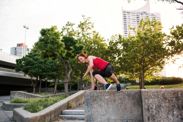 A young sportswoman outdoors in city, jumping from concrete wall.