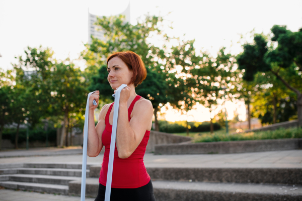 A portrait of young woman doing exercise outdoors in city with elastic bands.