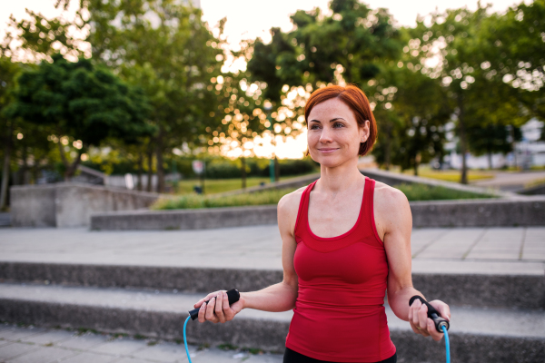 A young woman doing exercise outdoors in city with skipping rope.