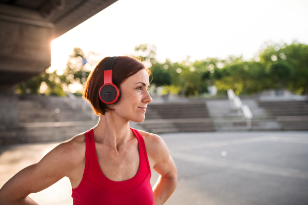 A young woman with headphones resting after doing exercise outdoors in city.