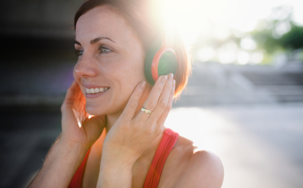 A close-up of young woman runner with headphones in city, listening to music and resting.