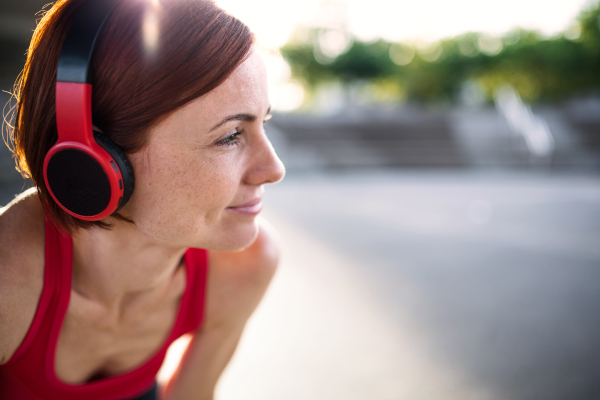 A young woman with headphones resting after doing exercise outdoors in city. Copy space.