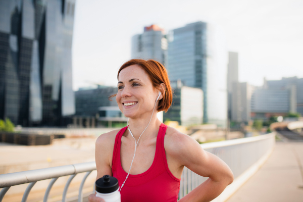 Young woman runner with water bottle in city, resting on the bridge. Copy space.