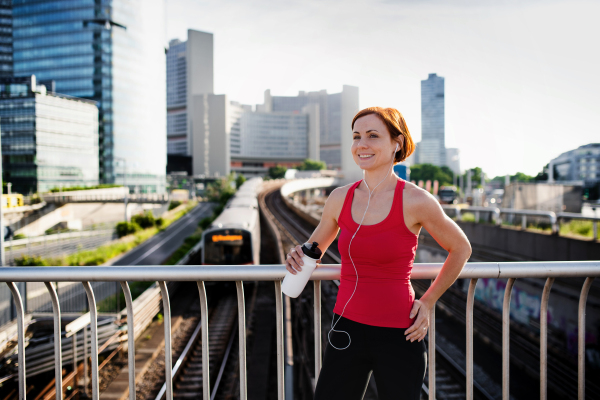 Young woman runner with water bottle in city, resting on the bridge. Copy space.