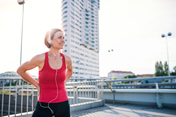 Young woman runner with earphones in city, resting on the bridge. Copy space.