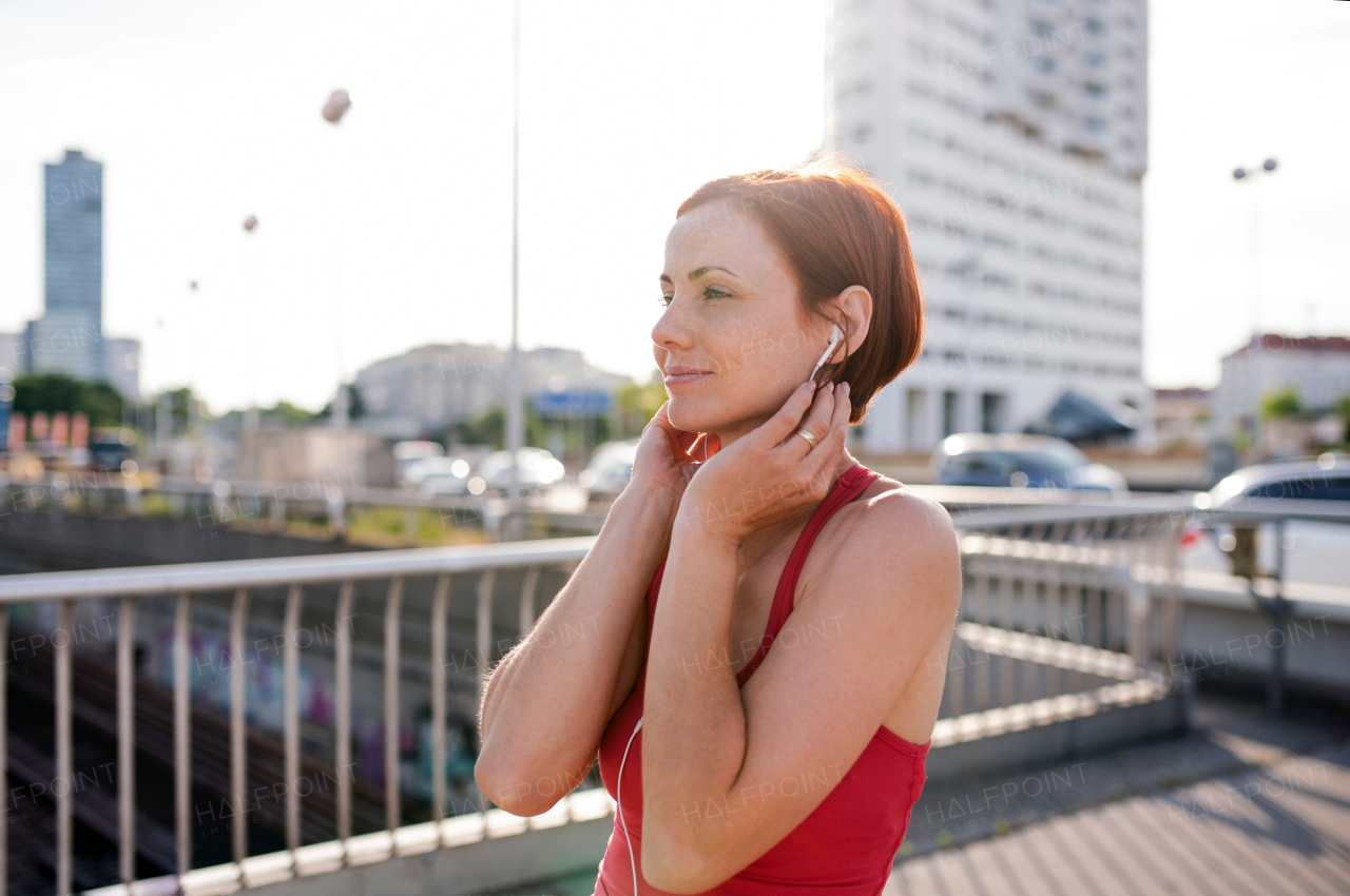 A young woman runner with earphones in city, resting on the bridge.