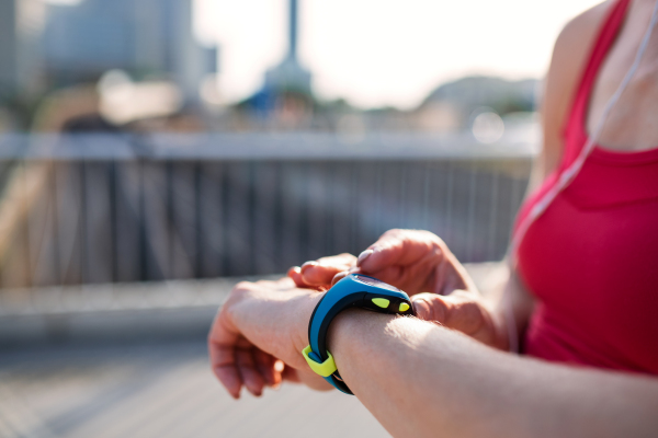 Midsection of young woman with smartwatch outdoors in city, resting after exercise.