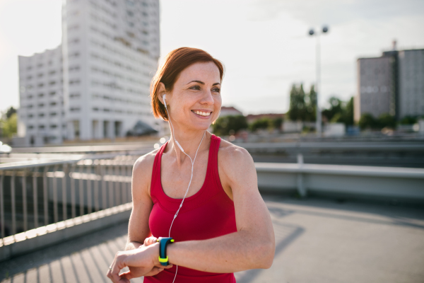 Young woman runner with earphones in city, using smartwatch when resting.