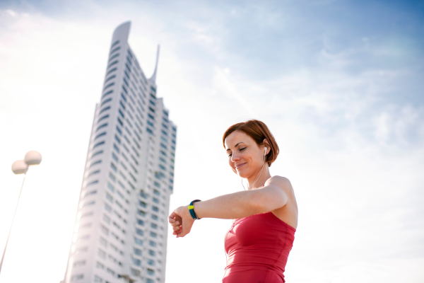 Low angle view of young woman with smartwatch outdoors in city, resting after exercise.