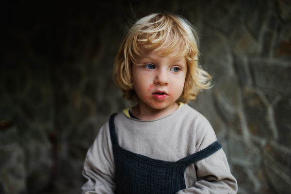 Front view close-up portrait of small boy standing outdoors, stone wall in the background.