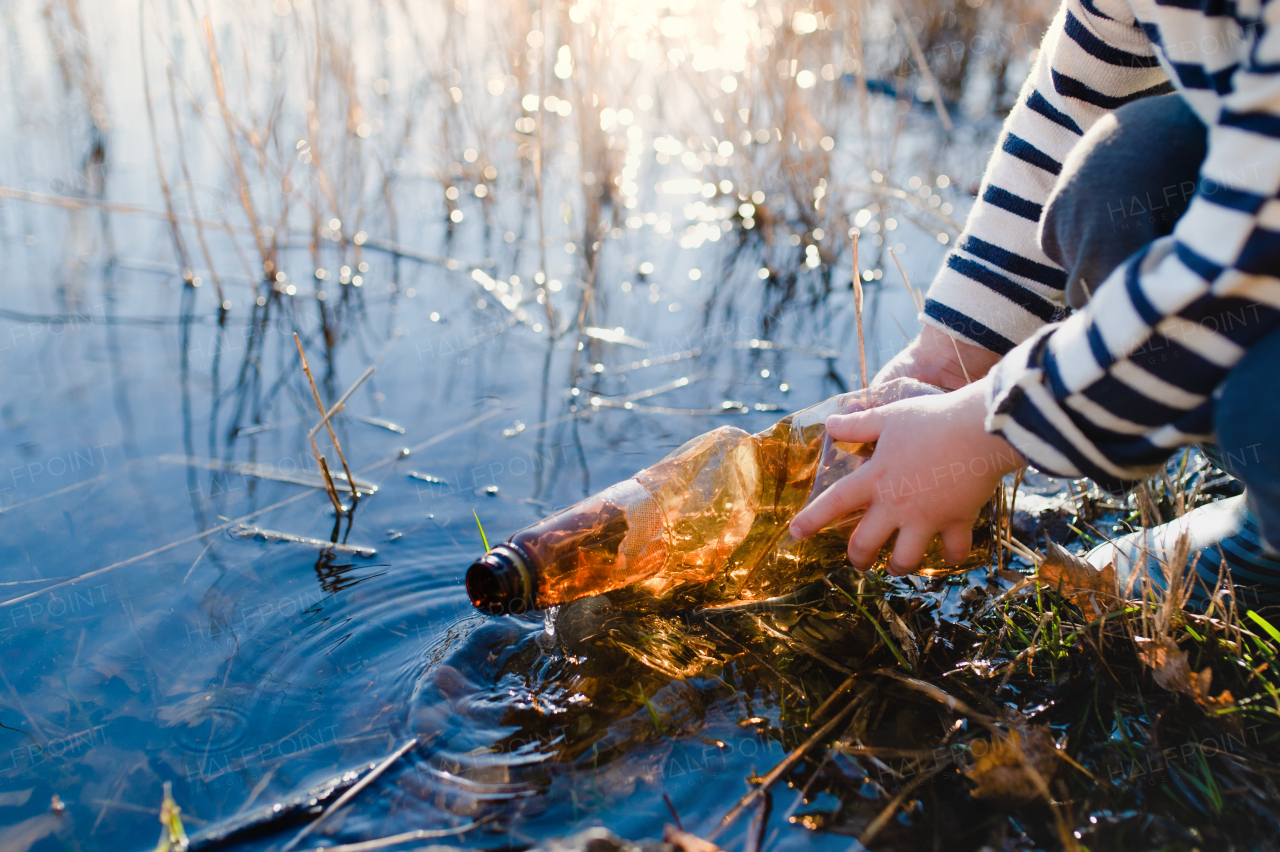 Midsection of unrecognizable small child collecting rubbish outdoors in nature, plogging concept.