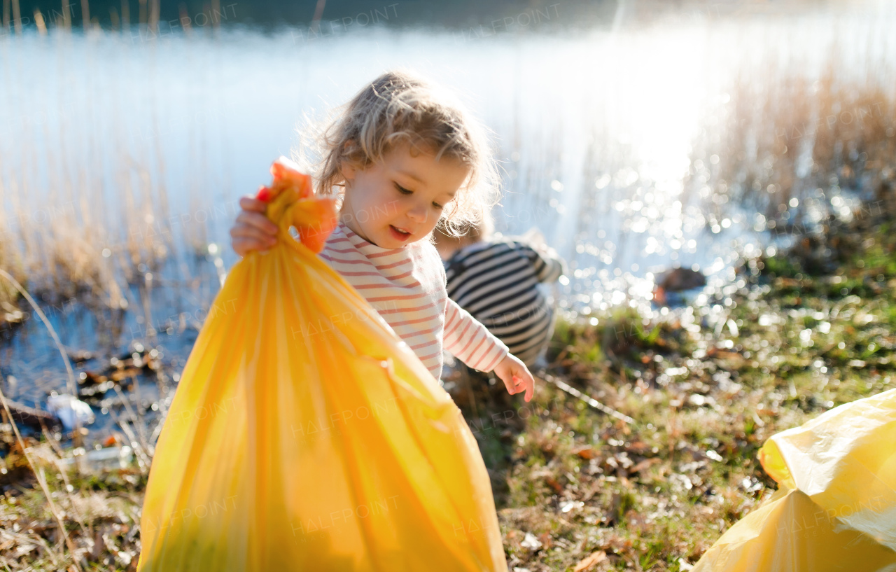 Small children collecting rubbish outdoors by lake in nature, plogging concept.