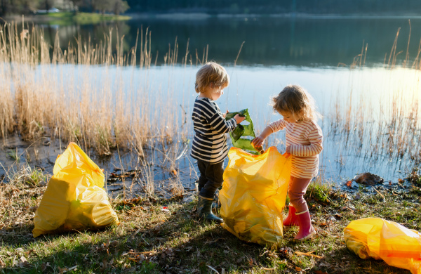 Small children collecting rubbish outdoors by lake in nature, plogging concept.