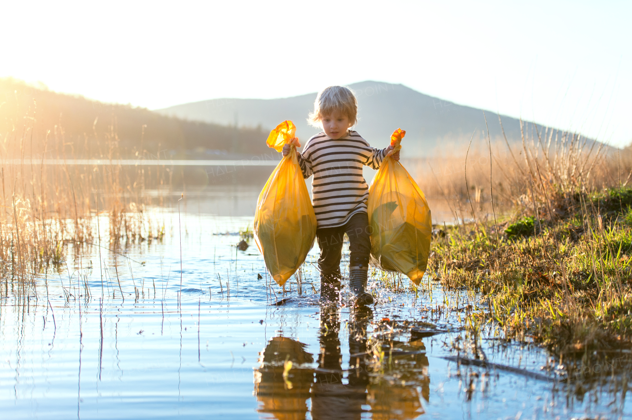 Small child collecting rubbish outdoors by lake in nature, plogging concept.