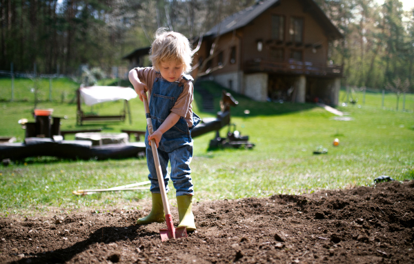 Happy small boy working outdoors in garden, sustainable lifestyle concept.