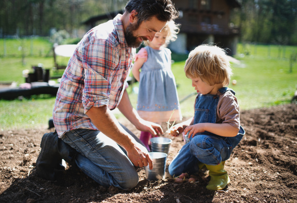 Mature father with small children working outdoors in garden, sustainable lifestyle concept.