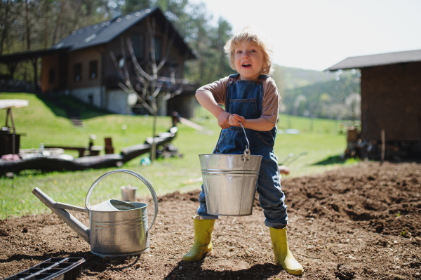 Happy small boy working outdoors in garden, sustainable lifestyle concept.