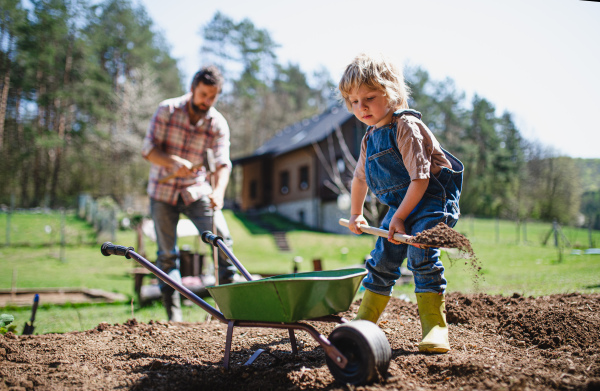 Mature father with small son working outdoors in garden, sustainable lifestyle concept.