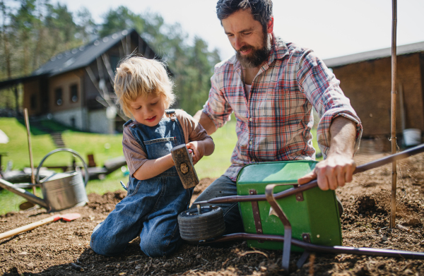 Mature father with small son working outdoors in garden, sustainable lifestyle concept.